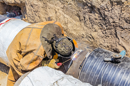 Welder welding a pipe on a terrain