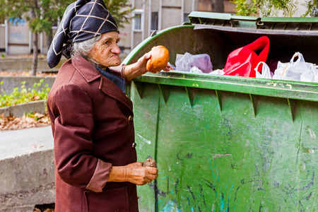 Homeless woman is searching for food in garbage. Woman in poverty is searching something in container.の写真素材