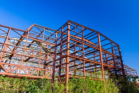 Old rusty abandoned industrial structure with beams and vegetation growing on it with a melancholic look suggesting long lasting work.の写真素材