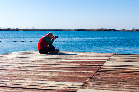 Photographer is take a photo sitting on the platform, shoots a lakeの写真素材