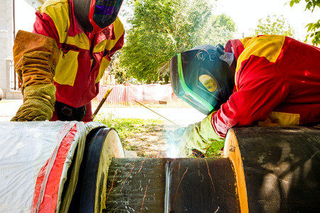 Welder working on a pipeline in construction site wearing overall and safety equipment