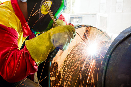 Welder working on a pipeline in construction site wearing overall and safety equipment