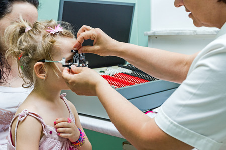 Young girl stand still while undergoing eye test with phoropter.の写真素材