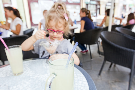 Little cute girl with glasses is eating ice cream at pastry shop in summertime.の写真素材