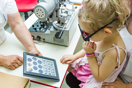 Optician in his surgery is giving girl eye test, treatment of eyesight by the oculist.の写真素材