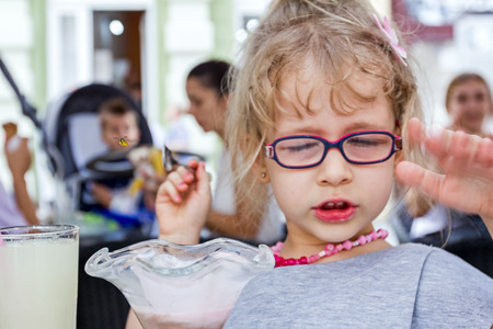 Little cute girl with glasses is eating ice cream at pastry shop in summertime.の写真素材