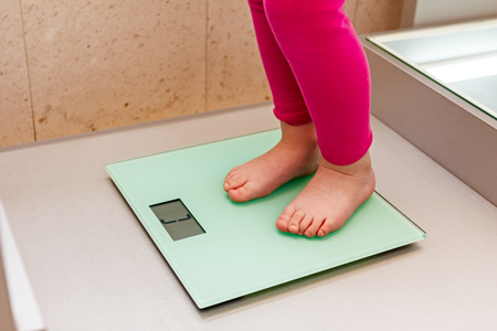 Child is with her bare feet standing on a bathroom slim scale of glass.の写真素材