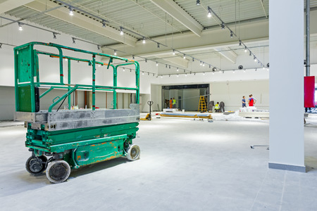 Scissor lift platform is inside of new big hall in building process.