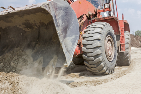 Red loader with wheels at earthmoving works. Bulldozer is pushing sand on huge pile.