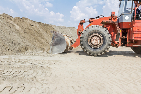 Red loader with wheels at earthmoving works. Bulldozer is pushing sand on huge pile.
