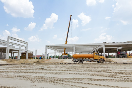 Mobile crane is carry concrete joist to assembly huge hall. Landscape transform into urban area with...