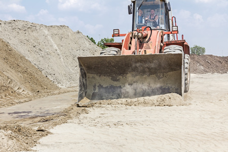 Red loader with wheels at earthmoving works. Bulldozer is pushing sand on huge pile.