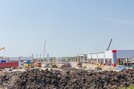 Mobile crane is carry concrete joist to assembly huge hall. Landscape transform into urban area with machinery, people are working. View on construction site.の写真素材