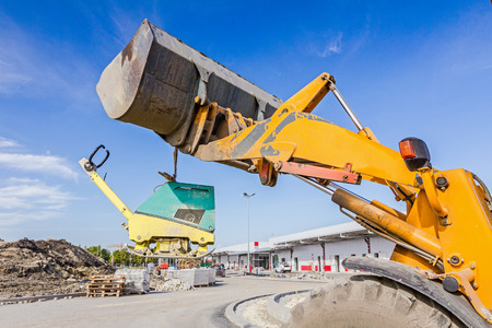 Excavator is moving over building site with raised up front bucket, vibration plate compactor...