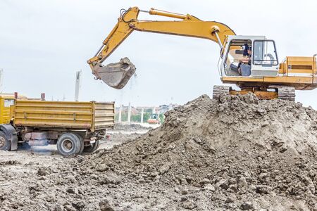 Yellow excavator is filling a dump truck with soil at construction site, project in progress.の写真素材