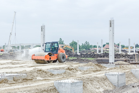 Steamroller is compacting sand among base pillars, passing over. Landscape transform into urban...