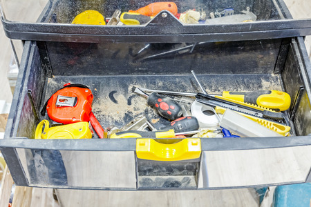 Variety of carpentry tools in tool box with open drawer on wooden floor.