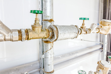 Water meters and valves in measuring place, tiled room with white tiles.
