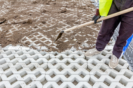 Workers are filling out symmetrical and decorative precast cobblestone shape with ground using...