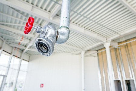 Red faucet from firefighter galvanized steel pipeline is hanging from ceiling.