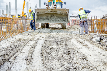 Workers are filling out with concrete armored shape, hole in ground using shovels.