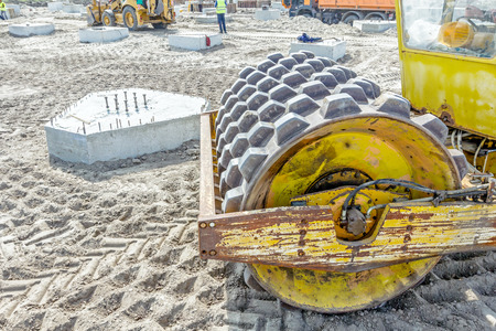 Construction worker is driving huge road roller with spikes and compacting soil for a large...