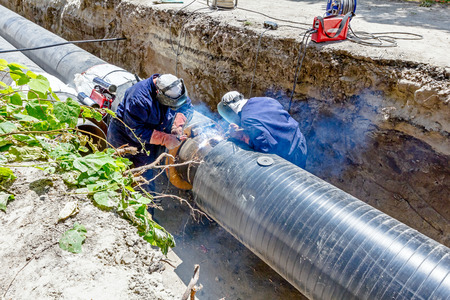 Team of welders is in trench working hard to install a new pipeline. Arc welding pipes