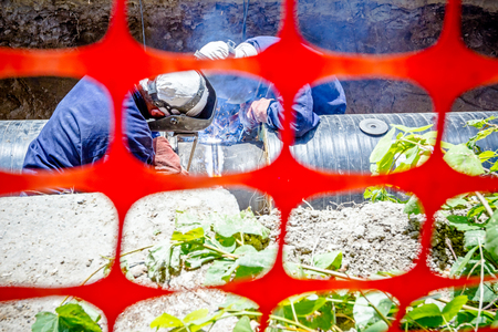 Welders are in trench they arc welding pipeline. Confined space with orange, plastic, safety netの写真素材