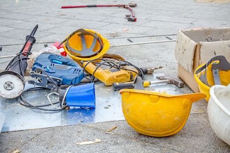 Hardhat and power tool are on the ground with plastic kettle for coffee or tea.