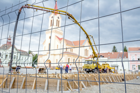 View on the pump crane for lifting and casting concrete at construction site through a fence wire with quadratic shape.の写真素材
