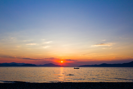 Silhouetted shot of beautiful sunset with fisherman boat on the waterの写真素材