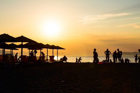 Silhouetted shot of sunset on the beach with people and sunshades, umbrellas for a perfect holiday.の写真素材