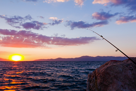 Fishing pole on a rocky beach, dock at purple sunset.の写真素材
