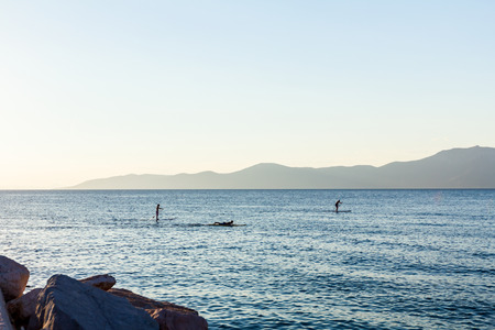 Silhouette of two surfers on paddle board are crossing over calm sea.の写真素材