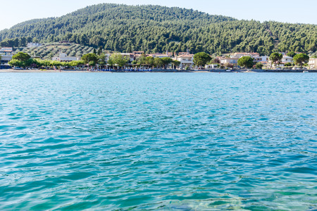 Low angle view on the stony beach with beautiful shallow turquoise water and town over sea.