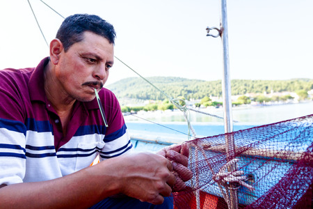 Pefki, Island Evia, Greece - 10, July 2017: Needle with thread in fisherman mouth until repairing net for angling.のeditorial素材