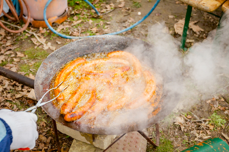 Hand with the help of metal tongs turns the simmering sausages on a black barbecue grill. の写真素材