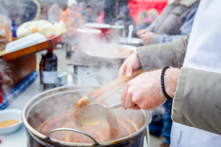 Hand with the help of metal tongs turns the simmering sausages on a black barbecue grill. の写真素材