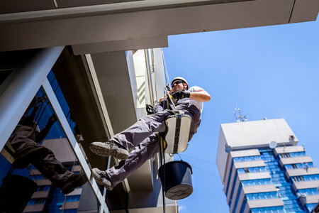 View from below on young man, industrial climber at work, he washing building facade.