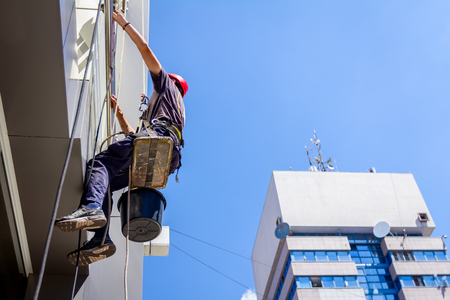 View from below on young man, industrial climber at work, he washing building facade.の写真素材