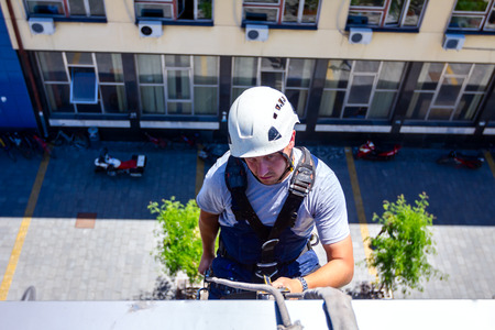 Industrial climber, alpinist, is passes over roof edge. He is climb down to wash building.