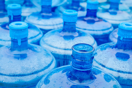 Big empty plastic water bottles for the cooler are stacked at outdoor warehouse.