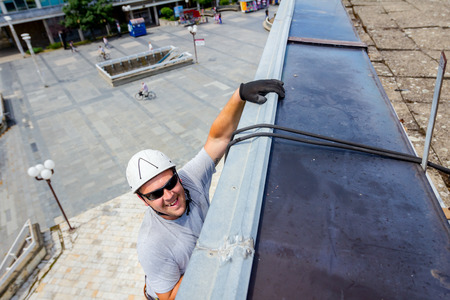 Industrial climber, alpinist, is passes over roof edge. He is climb down to wash building.の写真素材