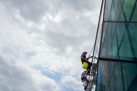 Industrial climbers are applying silicone to rubber juncture among building's glass facade.