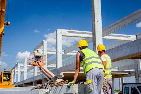 Worker is preparing crane hook for unloading concrete joist from truck trailer.の写真素材