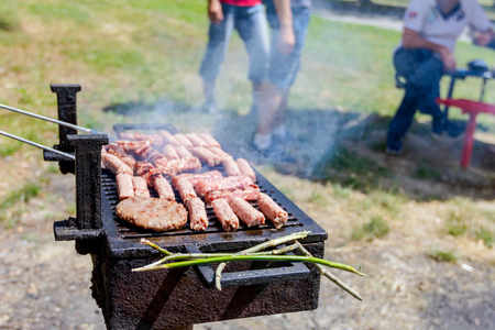 Hand with the help of metal tongs turns the simmering kebabs and burgers on a black barbecue grill.の写真素材