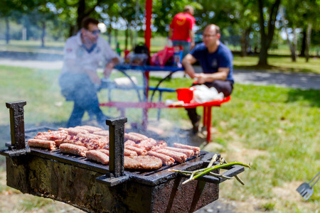 Hand with the help of metal tongs turns the simmering kebabs and burgers on a black barbecue grill.の写真素材