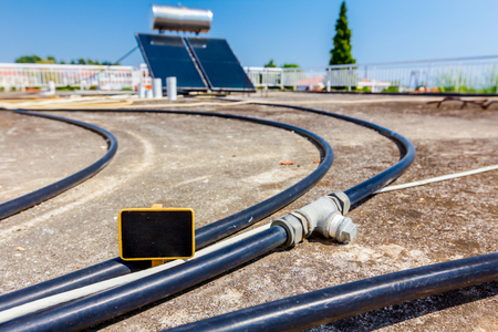 Empty small blackboard for message, among plastic hoses for supply water panels to using renewable sun energy are placed on house roof, solar hot system.の写真素材
