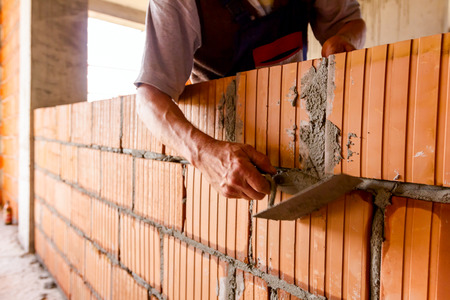 Worker is using spatula, trowel, to scrape off any excess mortar that spreads beyond the wall joint, bricklayer.の写真素材