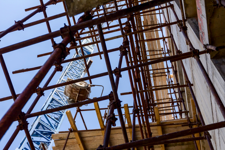 Crane is carry wheelbarrow, been pulled up on ropes above building site.